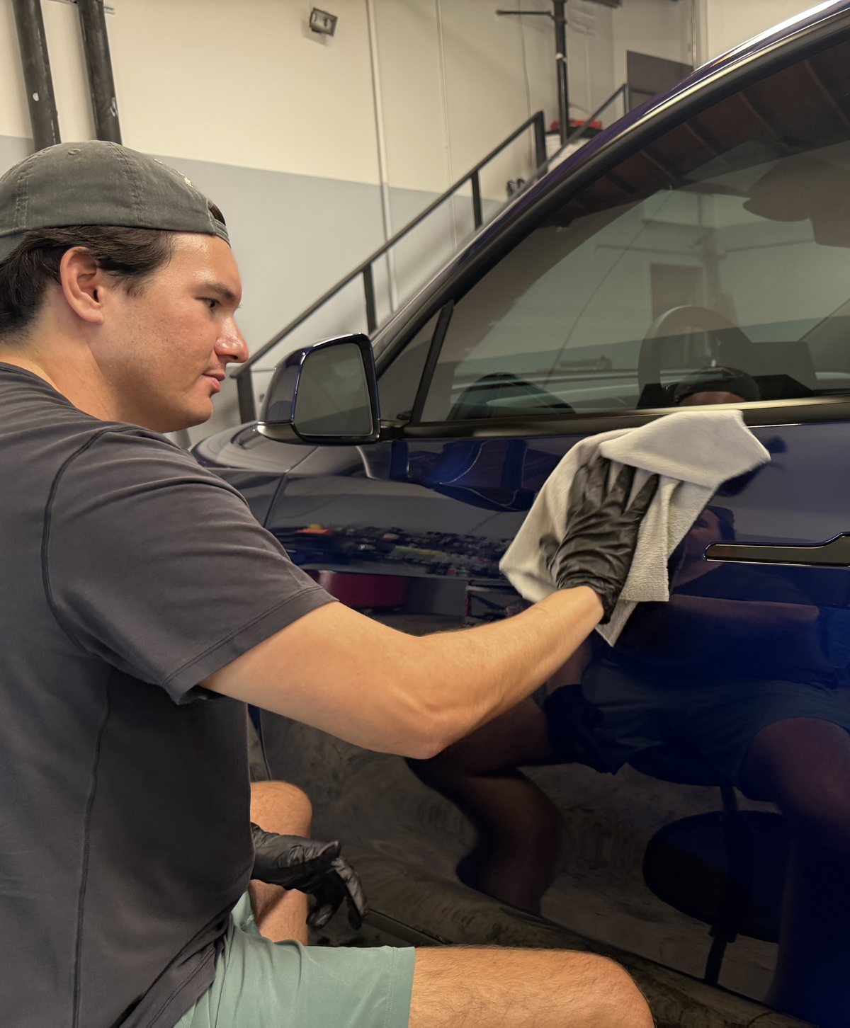Scott Wong, founder of Aloha Detail Center, wiping down the door of a dark blue SUV with a microfiber towel